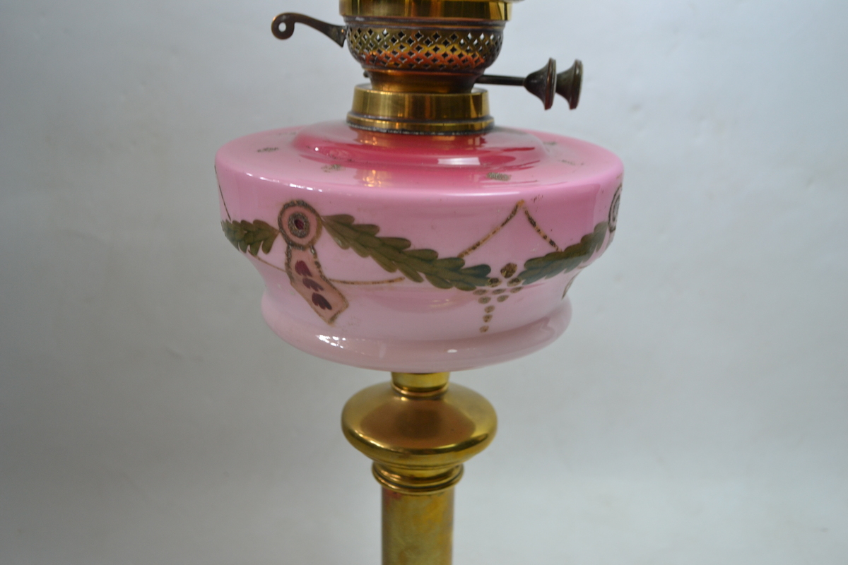 An Art Nouveau Brass Based Oil Lamp With Enamel Painted Cranberry Ceramic reservoir